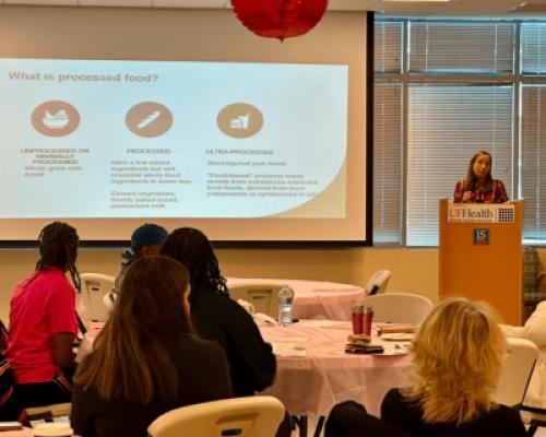 The audience of breast cancer survivors faces a projector screen and podium where Dr. Julie Bradley presents information about “Food as Medicine” 