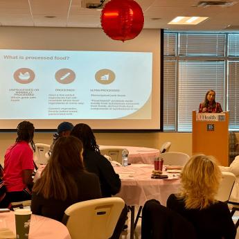 The audience of breast cancer survivors faces a projector screen and podium where Dr. Julie Bradley presents information about “Food as Medicine” 