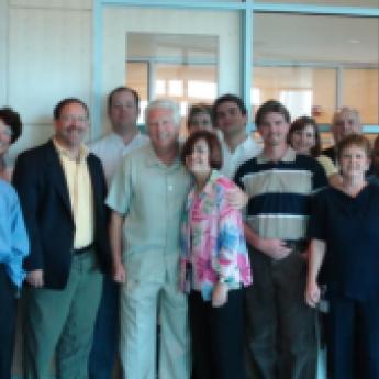 Group of men and women standing in a room with a glass wall in the background